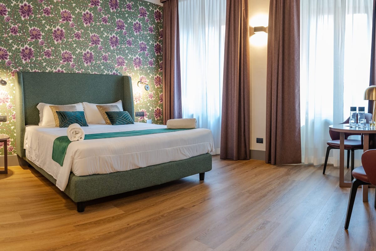 Ein Hotelzimmer mit einem großen Bett, einem Schreibtisch mit zwei Stühlen und Blick ins Freie durch das Fenster.