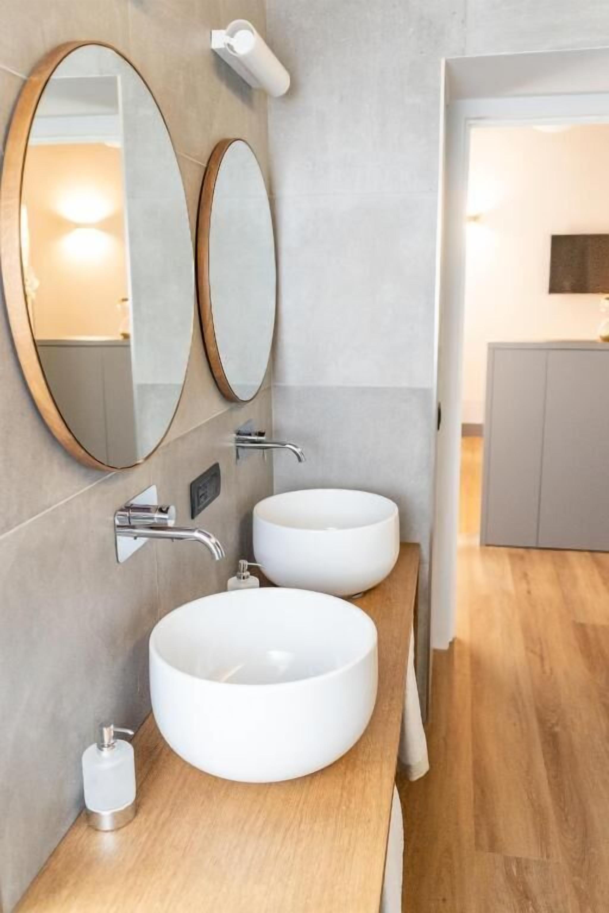 A modern bathroom with two round white sinks, a large mirror, and a handheld showerhead.