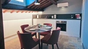 A compact kitchen with a dining area, featuring a modern stove, white cabinets, and red chairs. - Castel Sant Angelo Luxury Rooms & Tour (Rome)