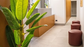 A reception area with a reception desk, a potted plant, and a hallway with red stools. - Castel Sant Angelo Luxury Rooms & Tour (Rome)