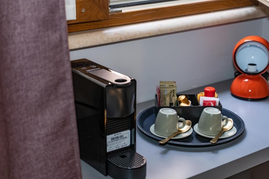 A compact kitchen area with a coffee maker, a tea kettle, and a tray with cups and condiments.