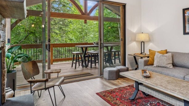 Ein modernes Wohnzimmer mit einem großen Glasfenster, das auf eine Terrassenanlage führt, einer Couch, einem Couchtisch und einer Lampe.