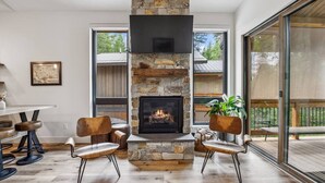 Ein modernes Wohnzimmer mit Kamin aus Stein, Holzboden und einer Glastür zu einer Terrasses.