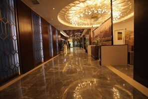 Un pasillo de hotel con piso de mármol pulido, una recepción y una lámpara decorativa en el techo.