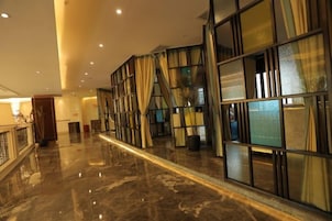 Un vestíbulo de hotel con piso de mármol, una escalera y un amplio ventanal con cortinas.