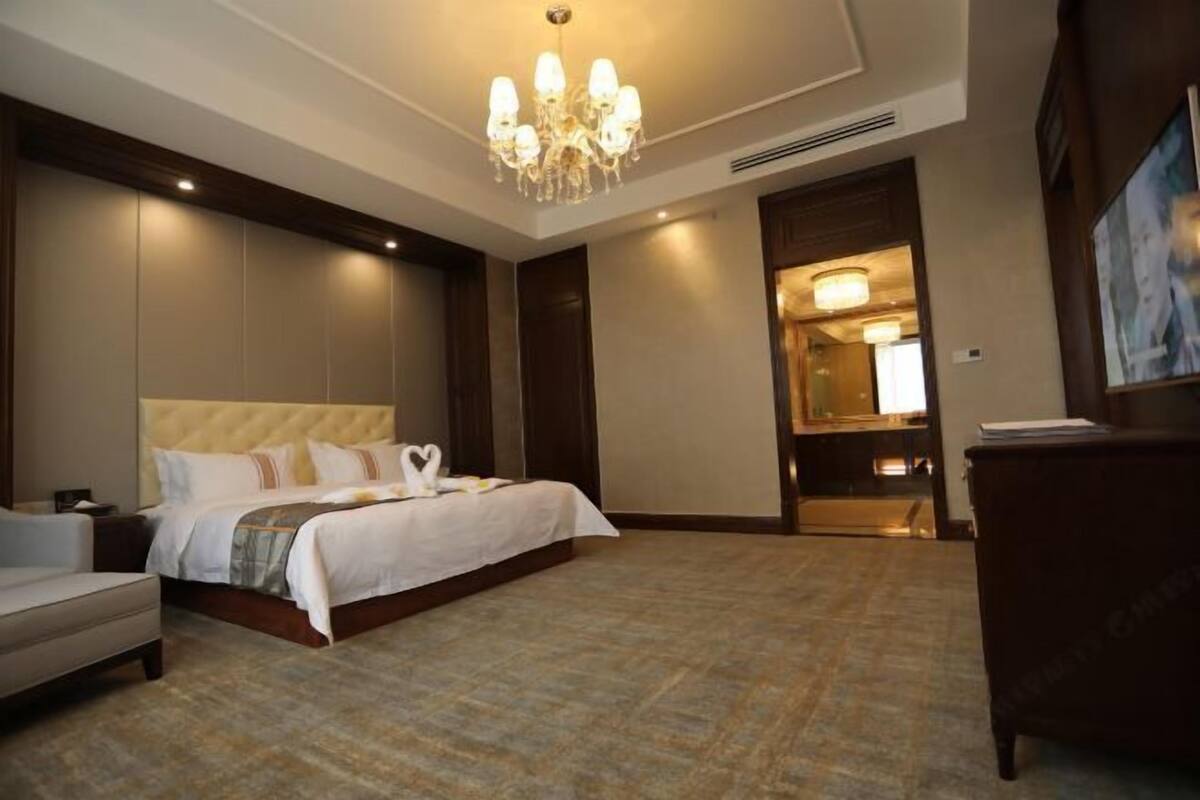 Una habitació d'hotel amb un llit gran, escriptori, cadira, un xandall i un quadre a la paret.