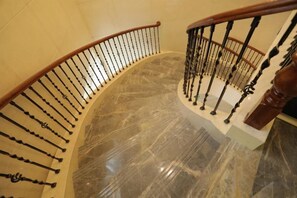 A curved staircase with a wooden handrail and metal balusters, marble flooring, and a beige wall. - Ruipu Hotel (Daozhen)