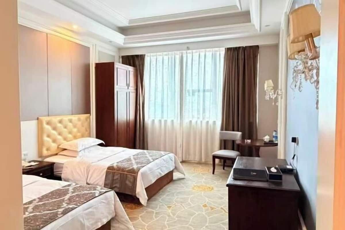 Una habitació d'hotel amb dos llits, una taula de treball, una cadira i un finestral gran amb cortines.