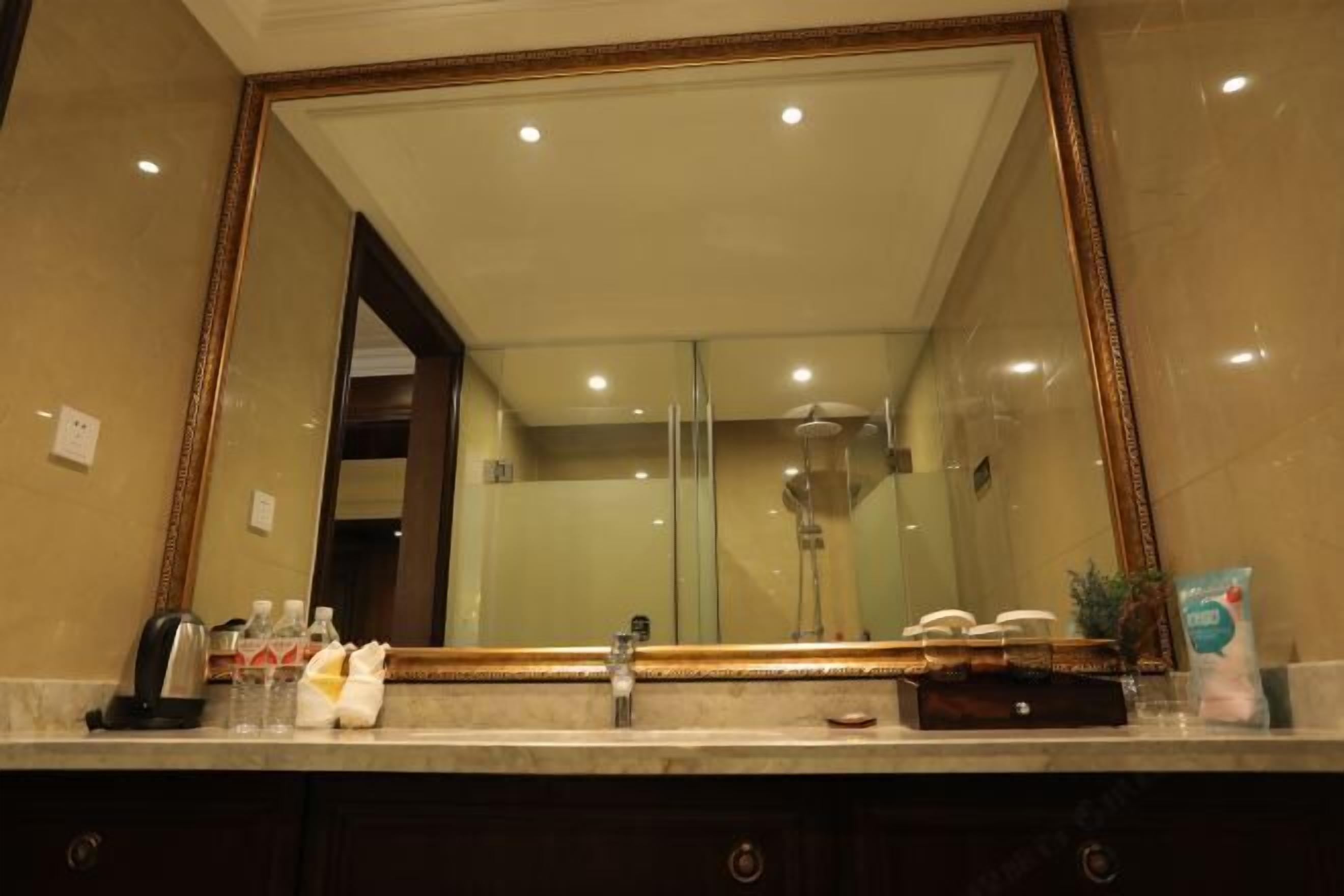 Une salle de bain avec un grand miroir, un lavabo et une douche, le tout visible dans le reflet.