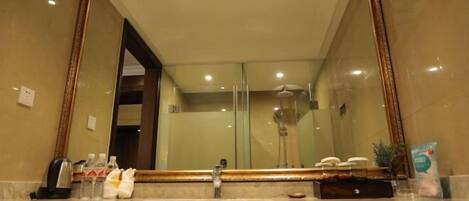 Une salle de bain avec un grand miroir, un lavabo et une douche, le tout visible dans le reflet.