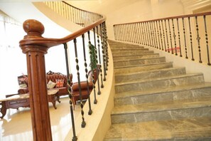 Un magnifique escalier en bois, doté d’une rampe et de balustrades noires, mène à un palier où se trouvent un canapé et un drapeau.