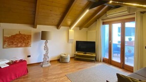 Un salon spacieux doté de parquets en bois, d’un canapé rouge, d’un téléviseur et d’une grande fenêtre agrémentée de rideaux.