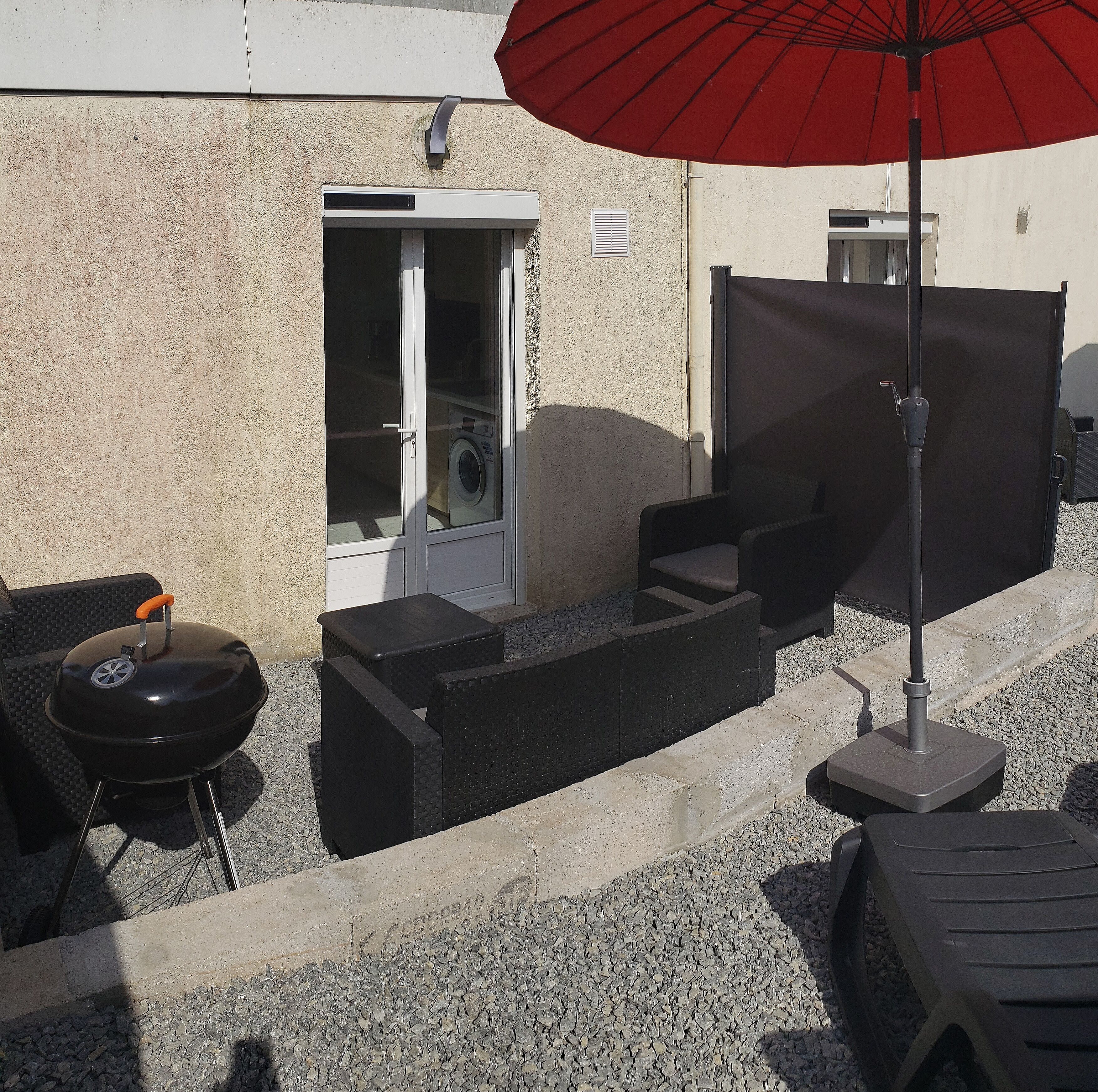 A patio area with a grill, outdoor seating, and a red umbrella.