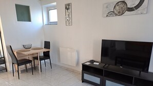 A modern living room with a flat-screen TV, a dining table with chairs, a black coffee table, and a black entertainment unit. - LOVELY, FULLY-EQUIPPED STUDIO WITH TERRACE 5 MINUTES' DRIVE FROM THE BEACH (Fouesnant)