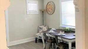 A dining area with a table set for four, a patterned armchair, and a wall clock. - Cozy Carriage House - Downtown (Colorado Springs)