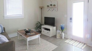 A living room with a sofa, a coffee table, a TV, and a door. - Cozy Carriage House - Downtown (Colorado Springs)