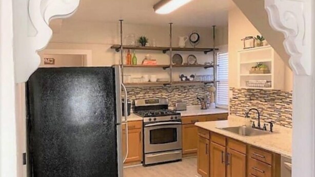 A kitchen with a black refrigerator, wooden cabinets, a stove, and a sink. - Cozy Carriage House - Downtown (Colorado Springs)