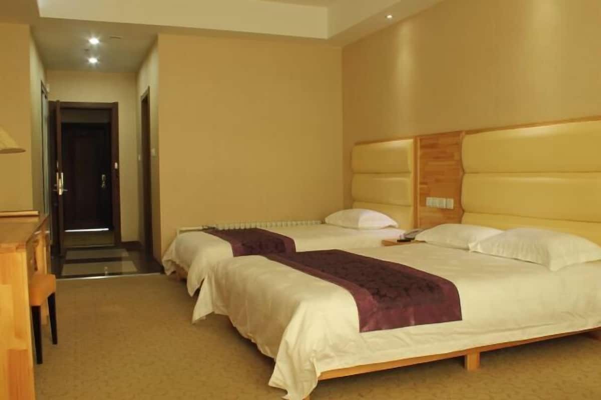 Een hotelkamer met twee bedden, een houten hoofdeinde, beige wanden en een vloerkleed.