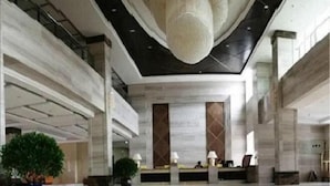 A spacious lobby with a high ceiling, marble walls, and a central reception desk.
