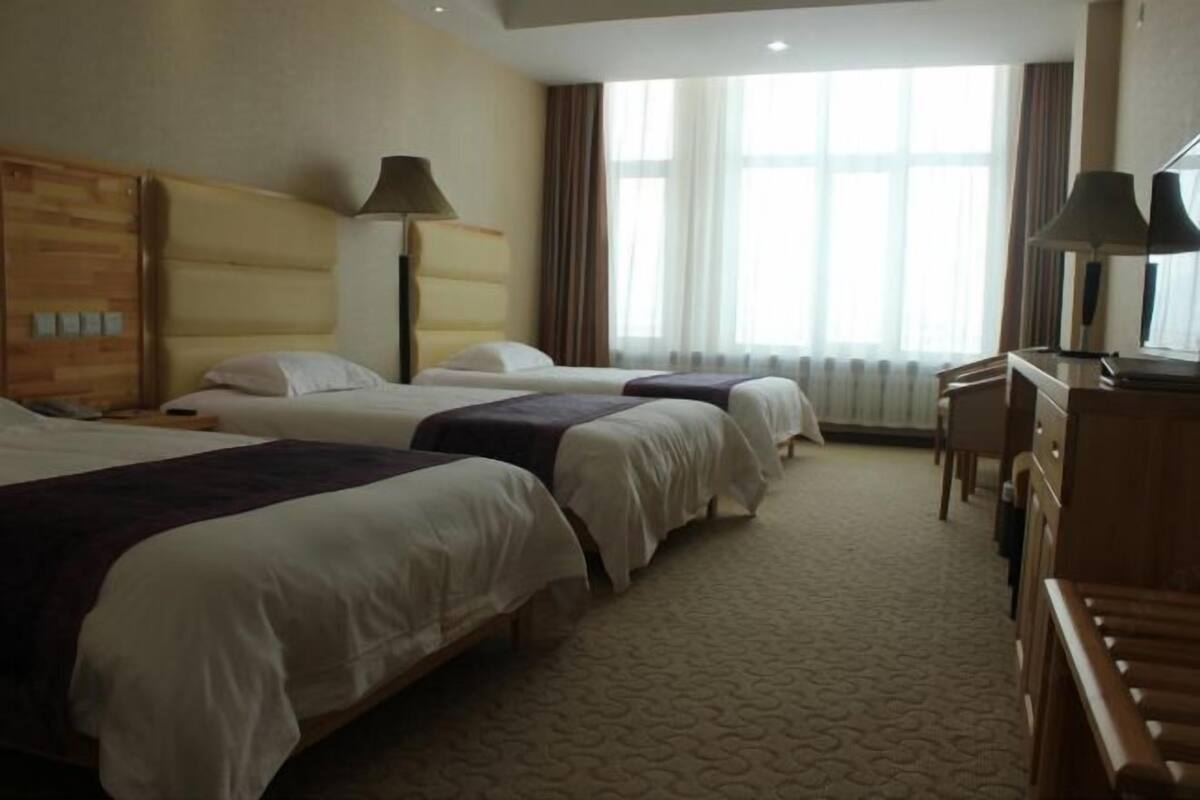 Een hotelkamer met drie bedden, een bureau en een stoel.