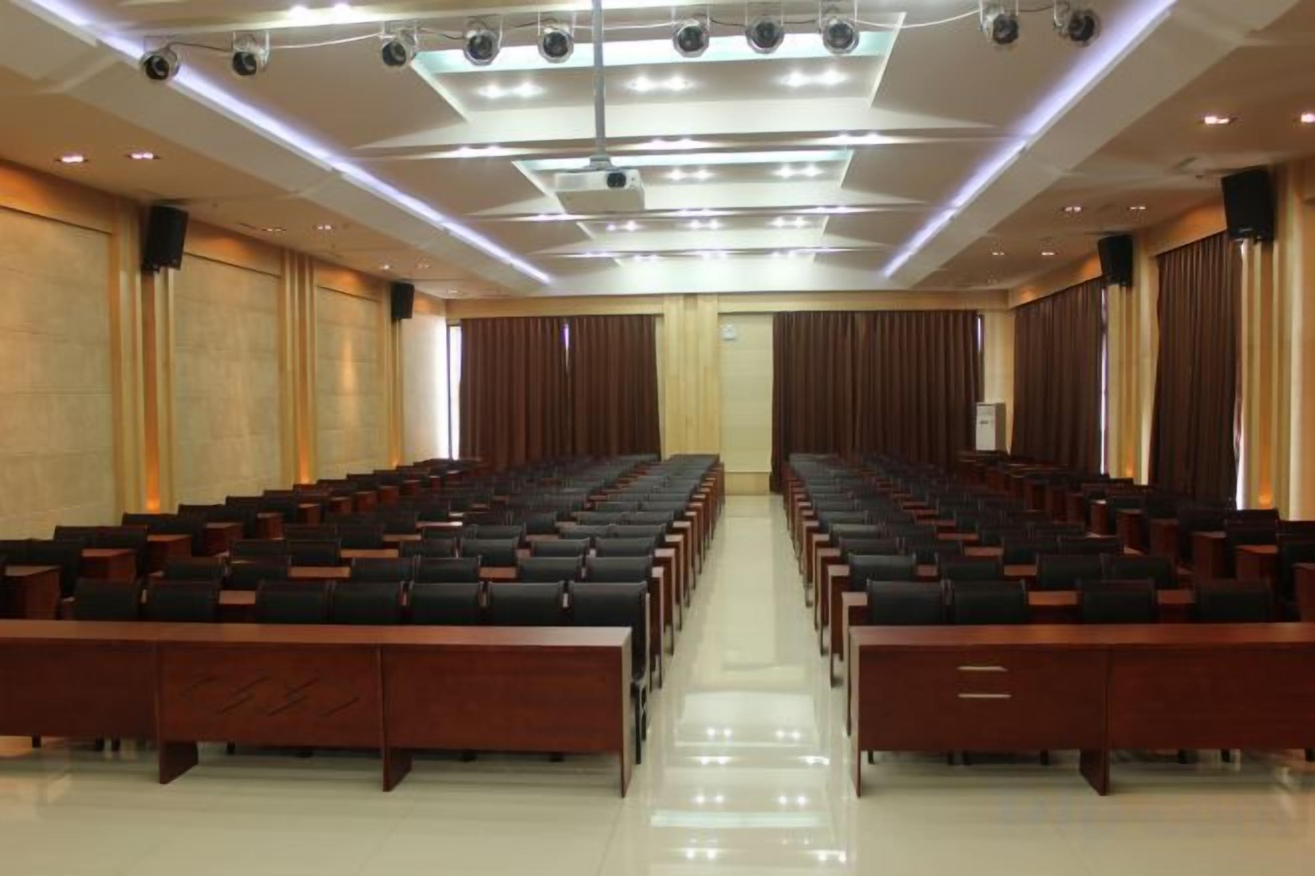 A conference room with rows of chairs, a stage at the front, and a large screen.