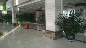A spacious lobby with marble flooring, large potted plants, and a high ceiling with exposed beams.