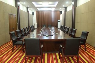 Un salón de conferencias con una larga mesa, varias sillas y piso alfombrado.