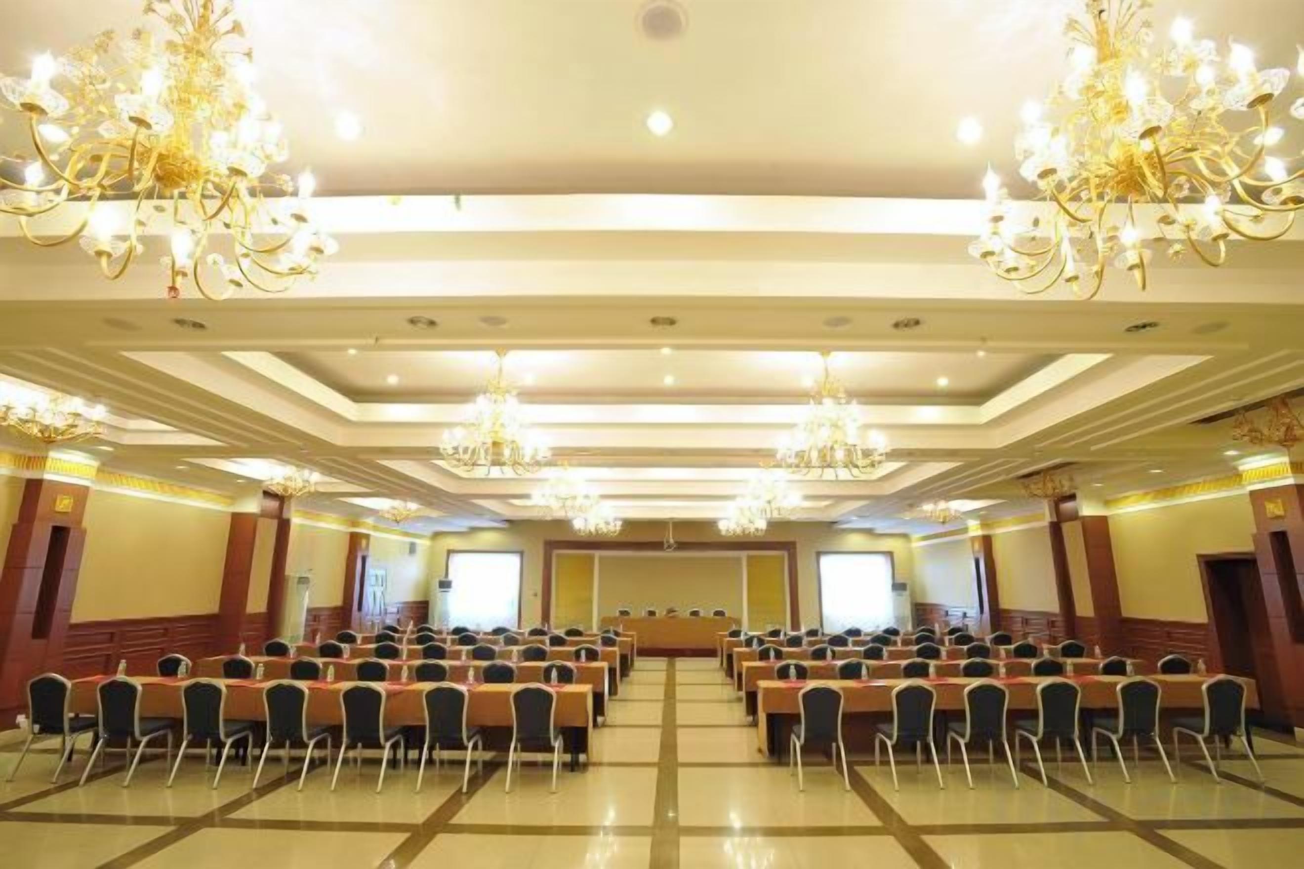 Un salón de conferencias con filas de sillas, candelabros y un escenario.