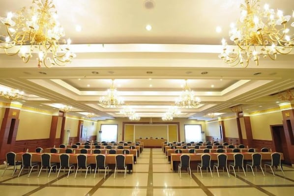 Un salón de conferencias con filas de sillas, candelabros y un escenario.