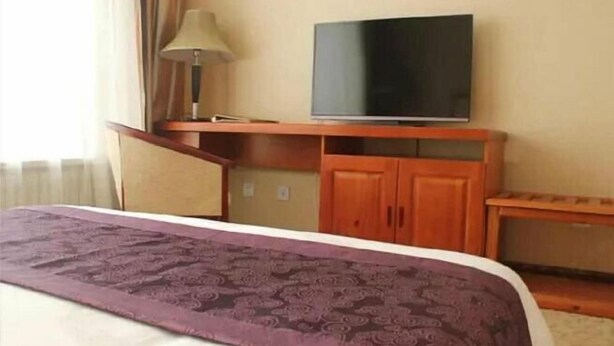 A hotel room with a bed, a television on a wooden stand, a lamp, and a small table.