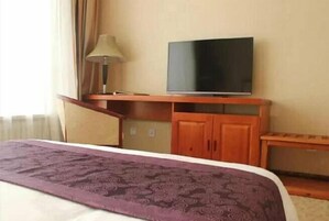 Una habitación de hotel con una cama, un televisor sobre un soporte de madera, una lámpara y una mesita.