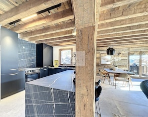 A modern kitchen with a marble countertop, wooden ceiling beams, and a dining area with a table and chairs.
