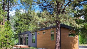 Una baita moderna con facciata in legno, un portico e un grande albero di fronte.