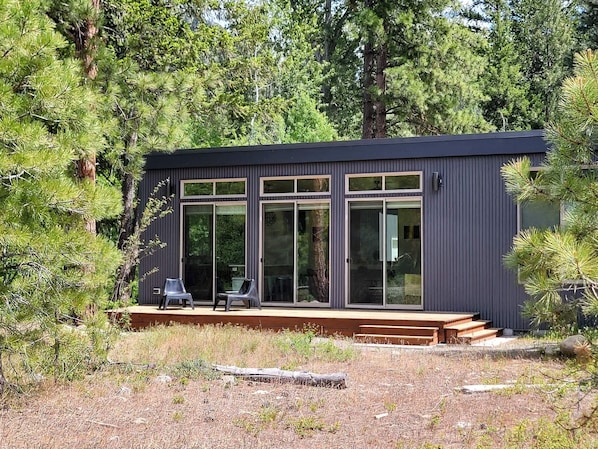 A modern cabin with large windows, a deck, and a forested backdrop.