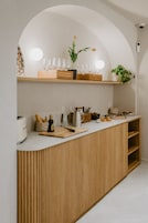 Una encimera de cocina con detalles de madera, una superficie de trabajo blanca y varios utensilios como una tostadora, pan y una tabla de cortar.