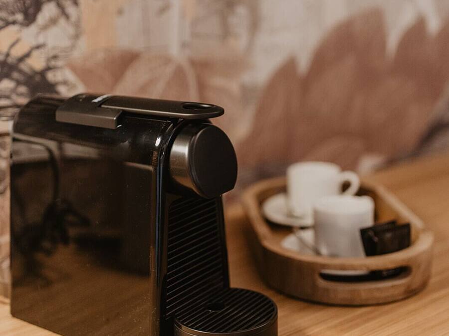 A coffee machine on a wooden table with a cup and saucer and a tray with more cups and a small item.