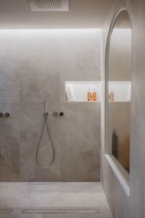 Een moderne douche ruimte met een glazen wand, een handdouche en een klein plankje met toiletartikelen.