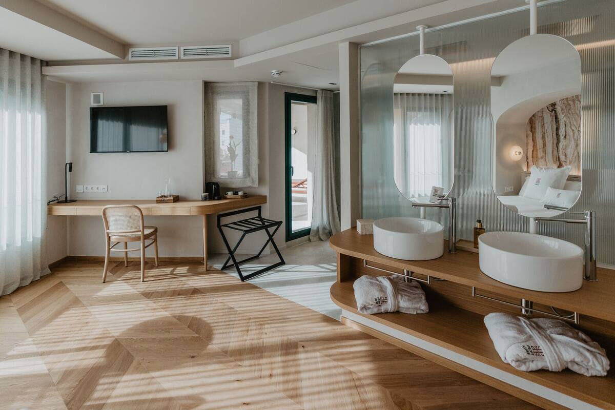 Een moderne hotelkamer met een houten bureau, een grote spiegel, twee ronde wasbakken en een houten vloer.