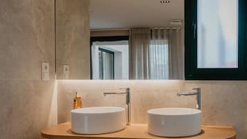 Un baño moderno con dos lavamanos redondos, un espejo grande y una ventana con cortinas.