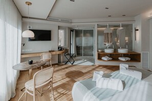 Een moderne hotelkamer met een houten bureau, een flatscreen televisie, een groot bed met witte lakens, een ingebouwde kaptafel met spiegel en een schuifdeur naar een balkon.