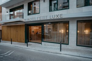 Fachada de hotel con una entrada amplia, un mostrador de recepción y un coche estacionado afuera.