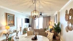 A dining area with a round marble table, beige upholstered chairs, and a chandelier.