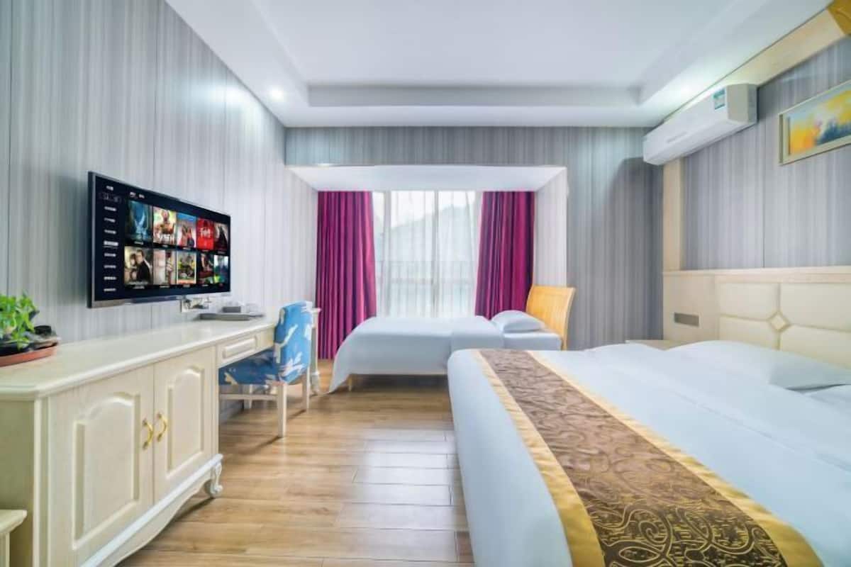 Ein Hotelzimmer mit Flachbildfernseher, einem Bett, einem Schreibtisch, einem Stuhl und einem Fenster mit Vorhängen.