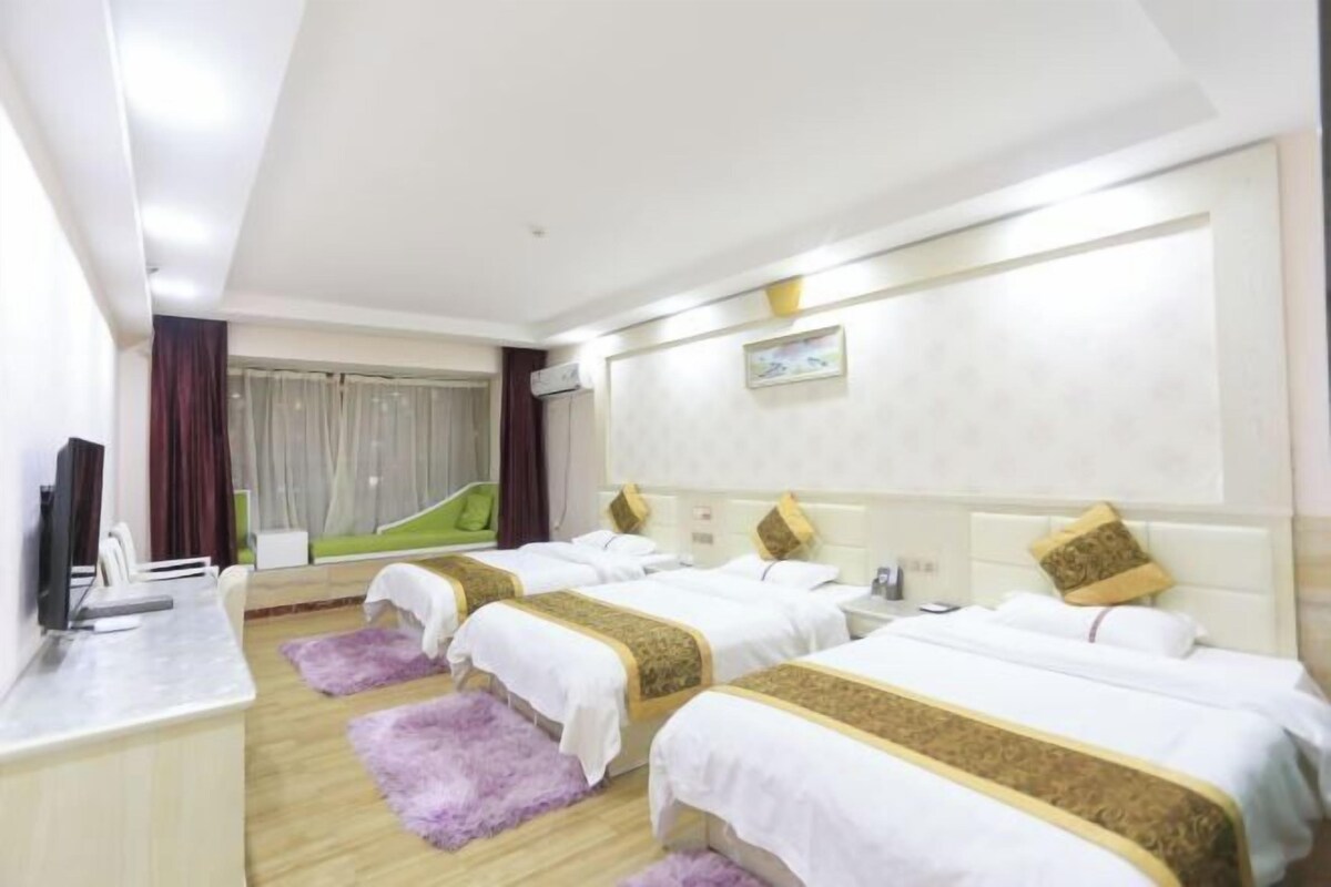 A hotel room with three beds, a desk, a television, and a window with curtains.