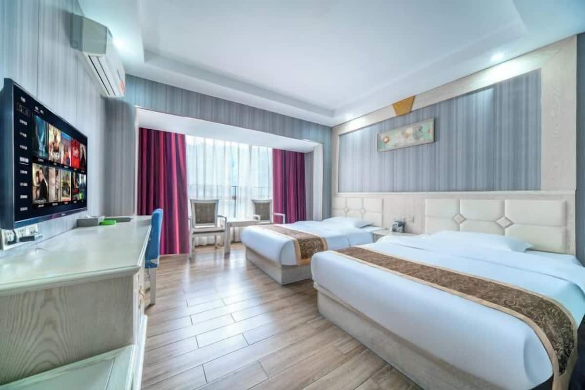 Ein Hotelzimmer mit zwei Betten, einem Schreibtisch, einem Fernseher und einem Fenster mit Vorhängen.