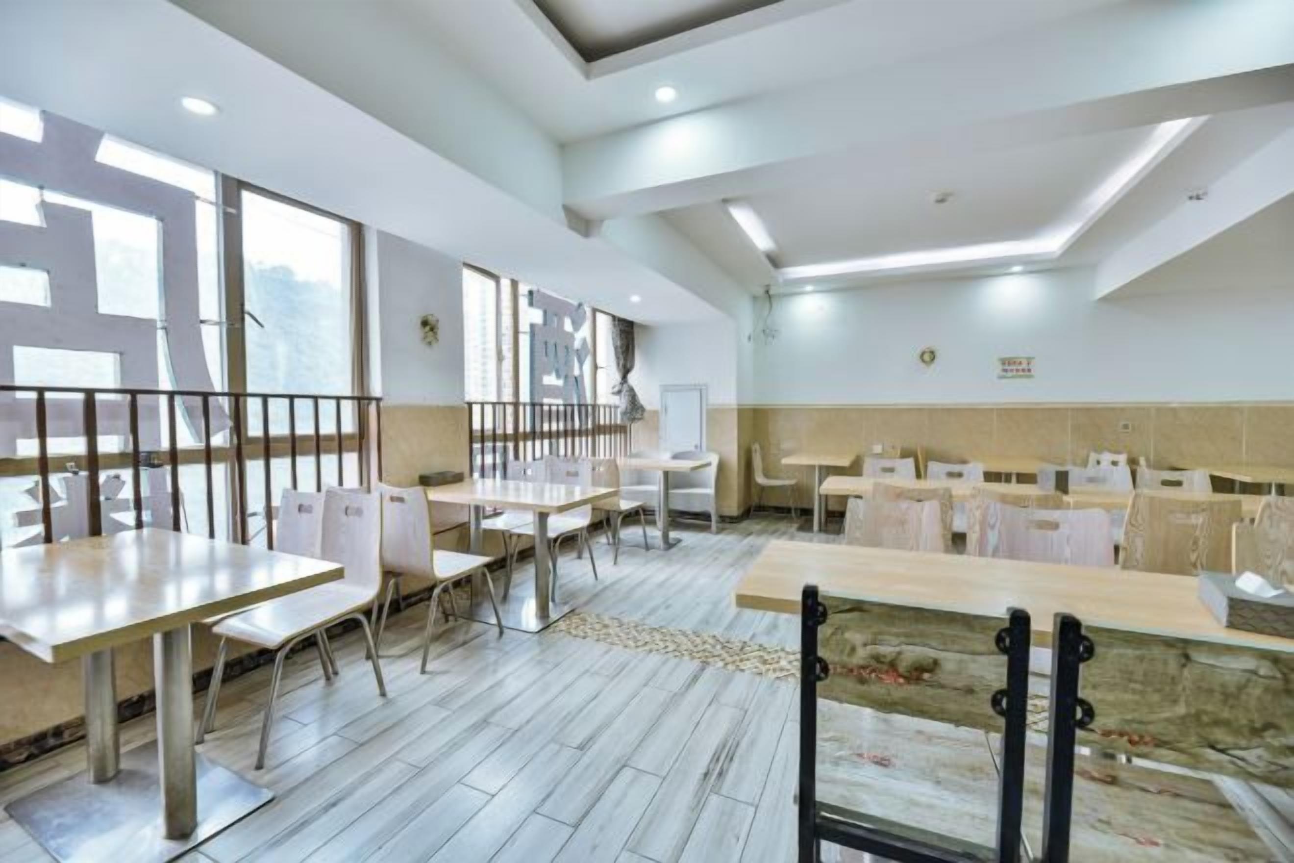 A spacious dining area with multiple tables and chairs, a high ceiling with recessed lighting, and a view through large windows.