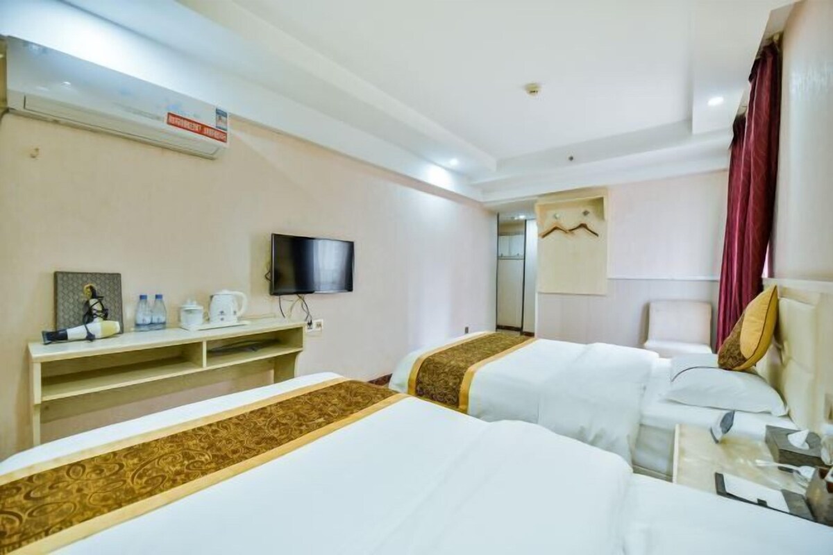 A hotel room with two beds, a TV, a shelf with toiletries, and a mirror.