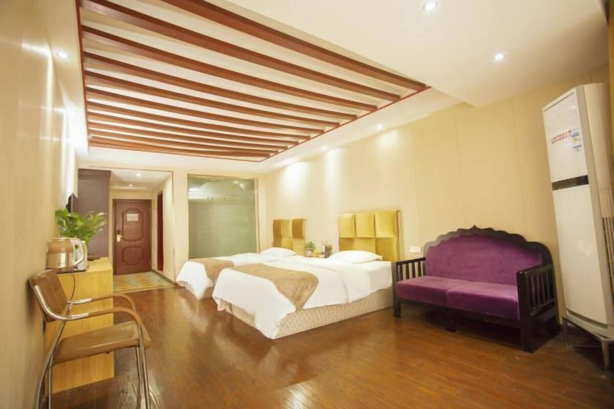 Ein Hotelzimmer mit Holzboden, einem Bett mit weißer Bettwäsche, einem violetten Sofa und einem kleinen Tisch mit einer Pflanze.
