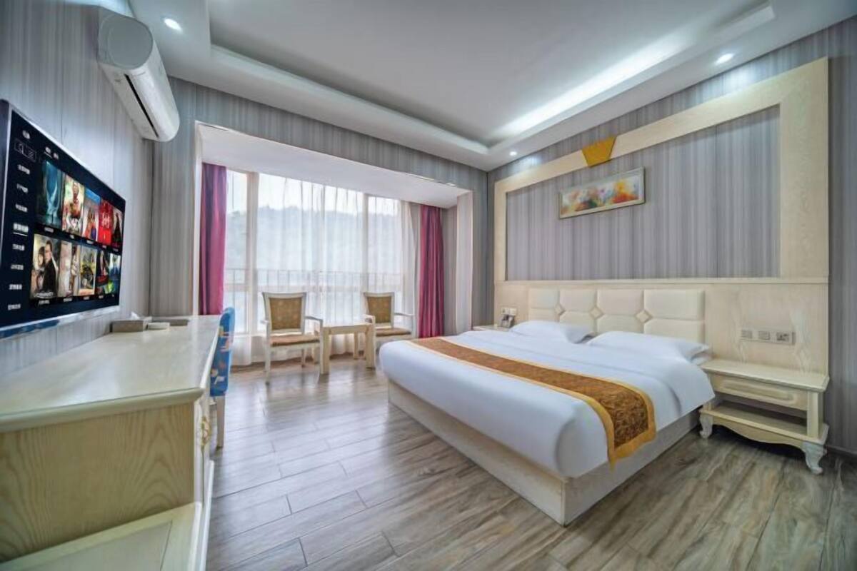 Ein Hotelzimmer mit einem großen Bett, einem Schreibtisch und einem an der Wand befestigten Fernseher.