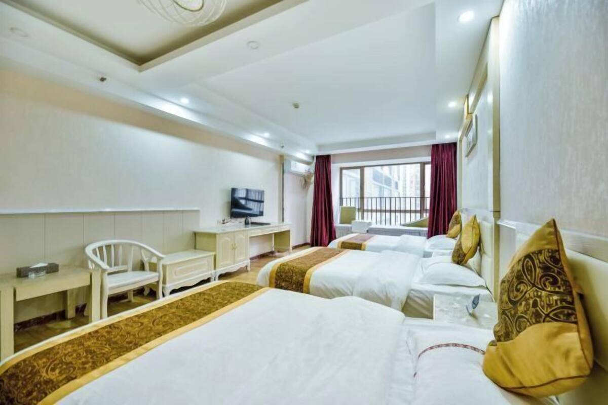 Ein Hotelzimmer mit drei Betten, einem Fernseher, einem Schreibtisch und einem Stuhl.